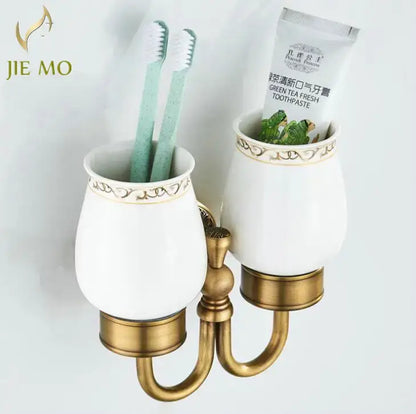 Ornate white ceramic double cup holder with gold detailing and brass base holding two mint green toothbrushes