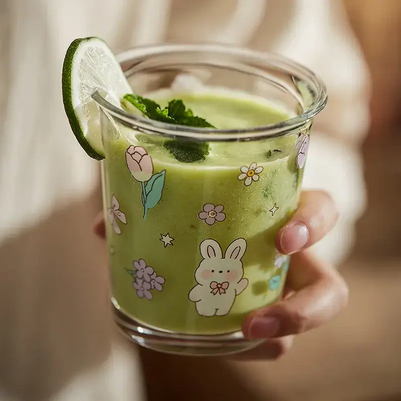 A clear bear rabbit glass tea tumbler with pastel floral decals holding a green smoothie garnished with mint and lime
