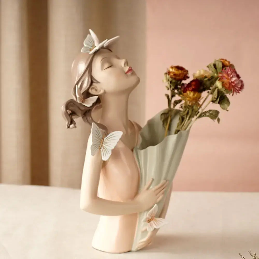 A delicate pastel green and peach girl vase statue featuring a porcelain pink butterfly girl with closed eyes and bouquet