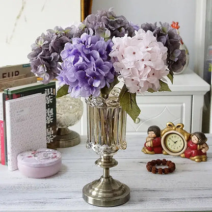 A decorbites hydrangea branch silk flower bouquet in pastel purple and pink arranged in an ornate silver vase for dining room decor