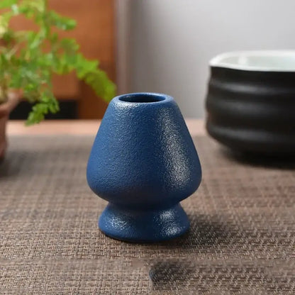 A matte blue ceramic tea bowl holder with a textured tapered body and flared base for matcha whisk stand use