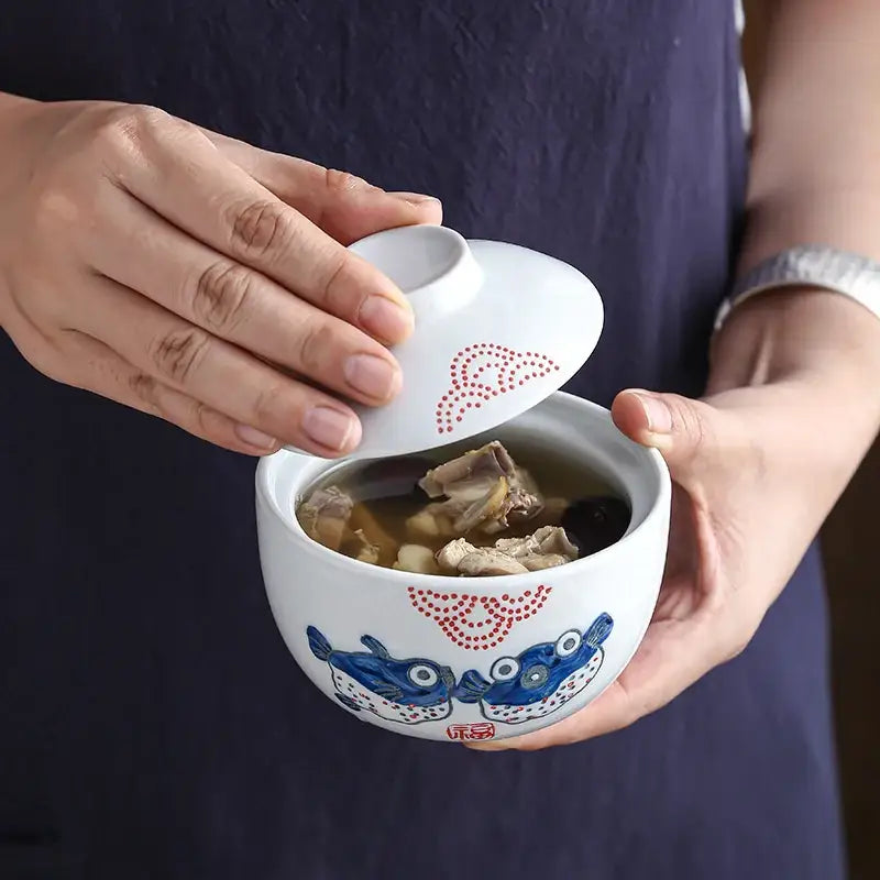 Patterned white and blue ceramic stew pot bowl with fish and red dot designs featuring a matching lid