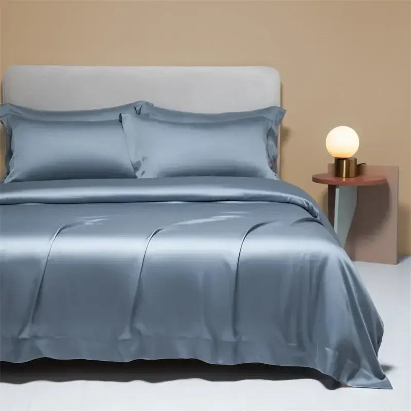 Silk satin duvet cover set in soft muted blue with elegant folds complements peach satin cooling cotton solid bedding set