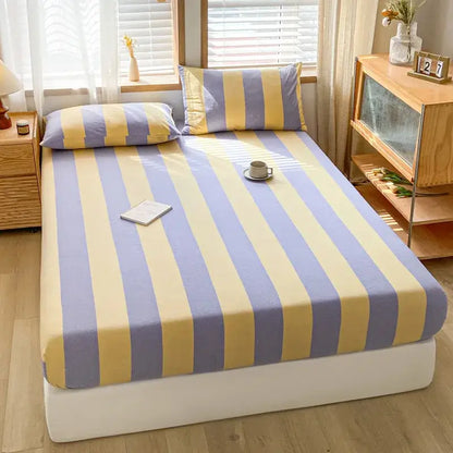 A cozy bed with a lavendar and yellow striped decorbites cotton stripe fitted sheet and matching pillowcases