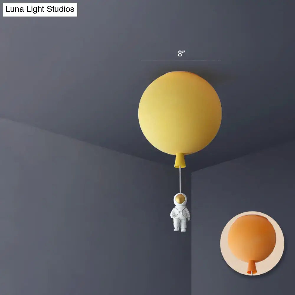Yellow balloon-shaped ceiling lamp with small astronaut figurine hanging below pink and blue astronaut ceiling lamp