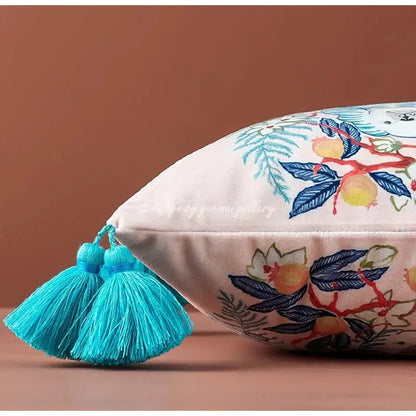 Cream-colored lumbar pillow cover with embroidered botanical patterns and turquoise tassels featuring blue lion dog decor