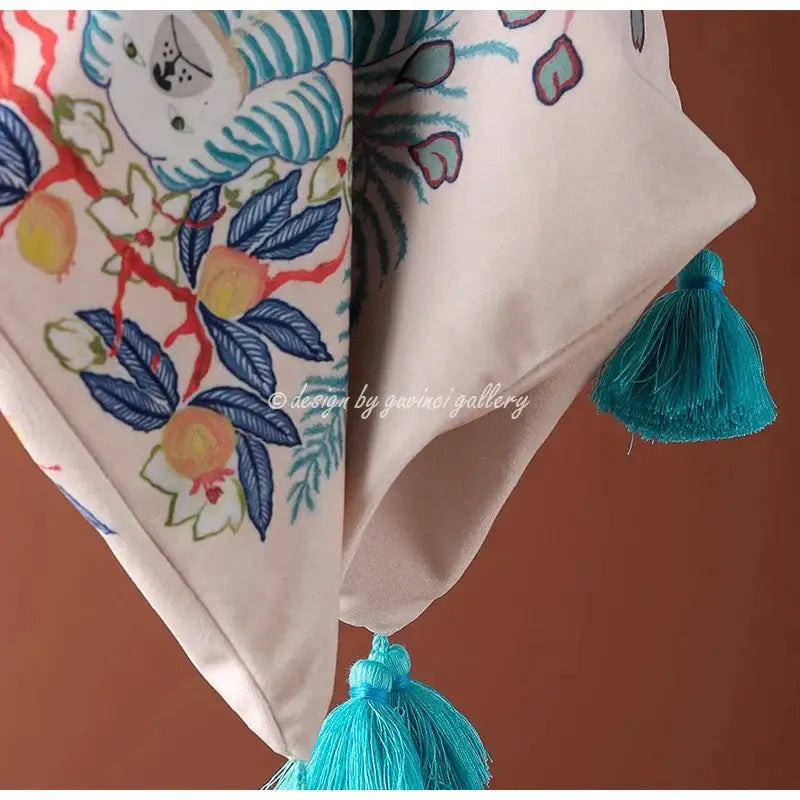 A cream scarf with embroidered blue lion dog foliage blossoms and a whimsical white tiger with turquoise tassels