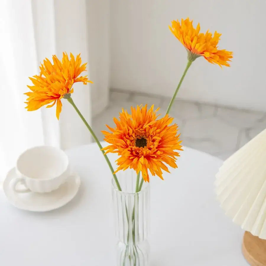 A clear vertically ribbed glass brushed gerbera vase holding three vibrant orange gerbera daisies for living room decor