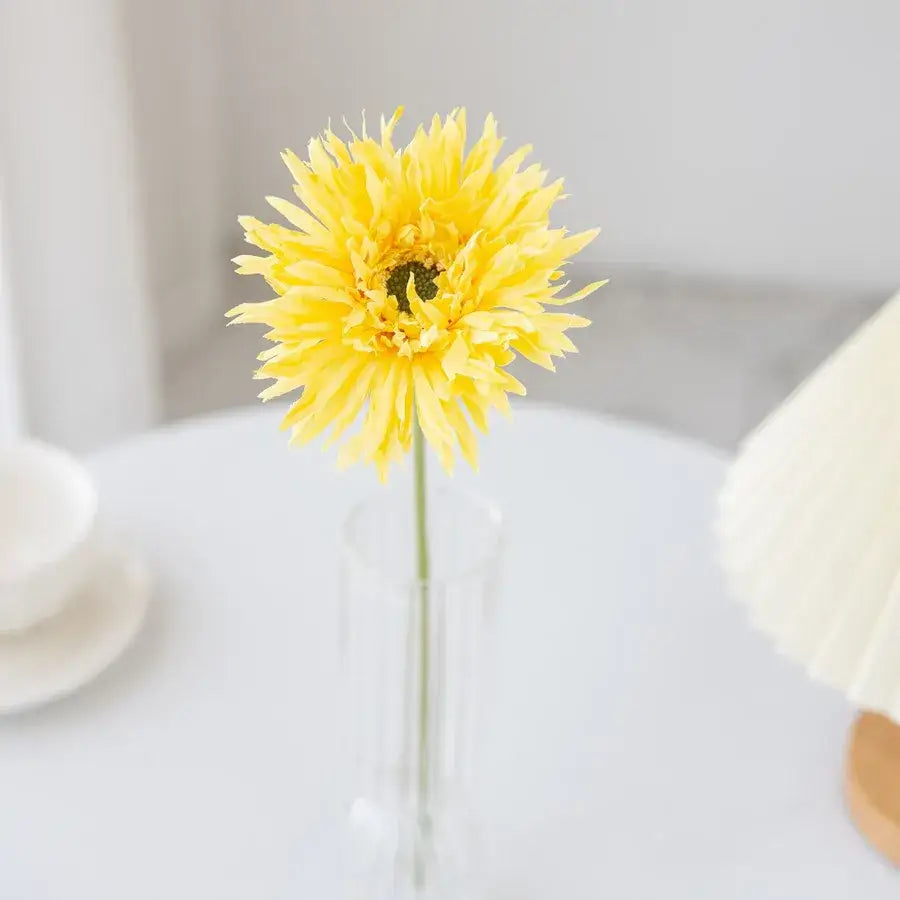A vibrant yellow artificial gerbera with spiky petals in a slender clear glass brushed gerbera vase for living room decor