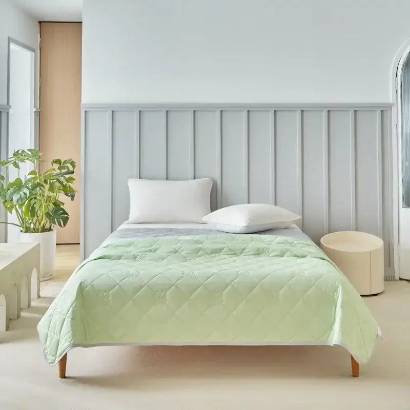 Light green quilted cool summer blanket with subtle diamond pattern draped over wooden bed frame for cooling comfort