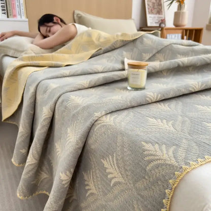 A soft gray and gold leaf-patterned decorbites cotton towel blanket with textured weave and fringed edge for bedroom decor
