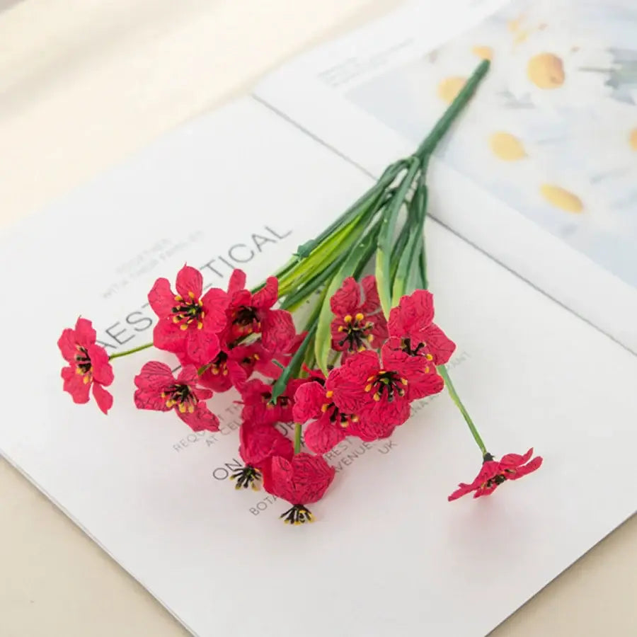 A cluster of vibrant red artificial cherry blossoms with textured petals and yellow stamens in a square box wedding decor