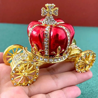 A shiny red and gold jeweled carriage ornament with crystal embellishments on a pink and white rhinestone jewelry trinket box