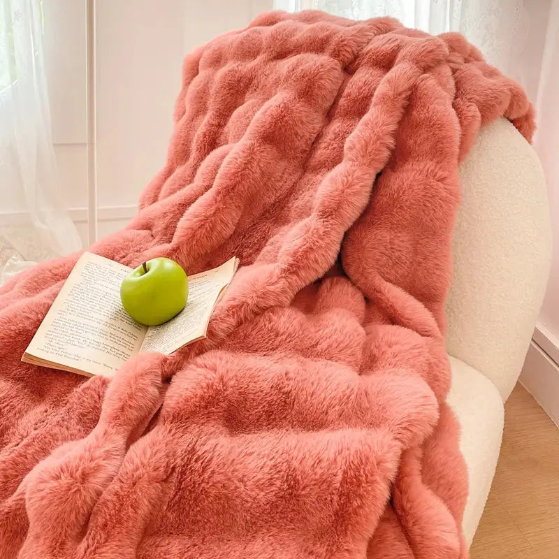 A plush cream and gradient pink double layer faux fur throw blanket with a textured wavy pattern draped over an armchair