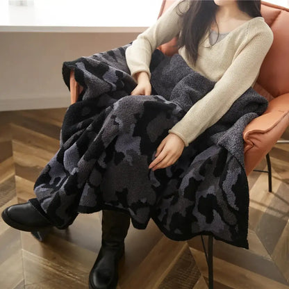 A plush dark gray and black camouflage knitted throw blanket draped over a person’s lap for cozy use