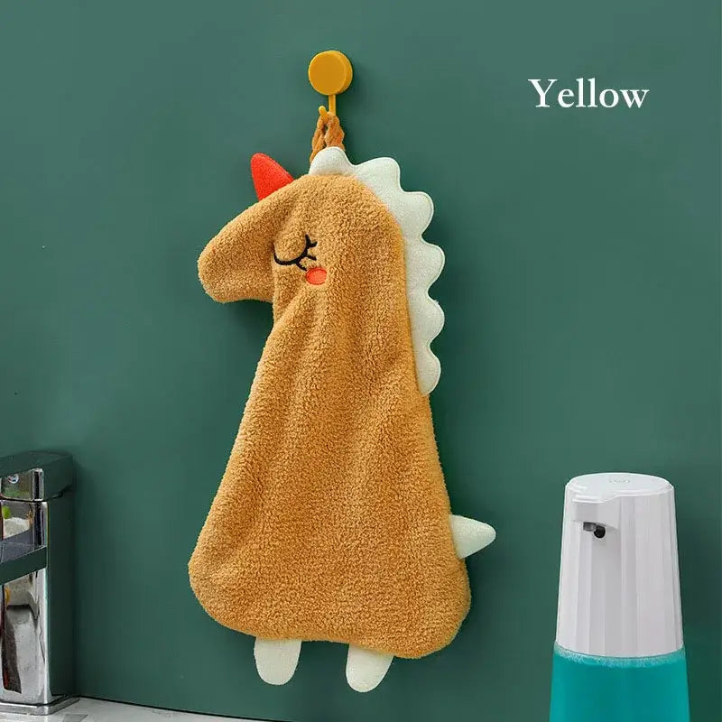 A plush tan dinosaur-shaped hand towel with white spikes and red horn made of double-layer coral velvet hanging on a hook