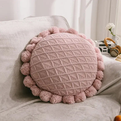 A soft pink knitted round pillow with textured diamond pattern and pom-pom trim for home decor and decorbites 3d flowers pillows
