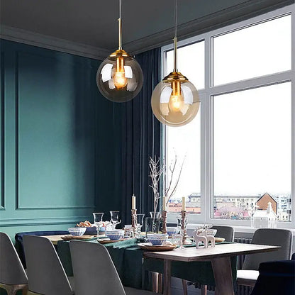 Two modern glass pendant lights with polished steel gold-toned fixtures hang above a dining table