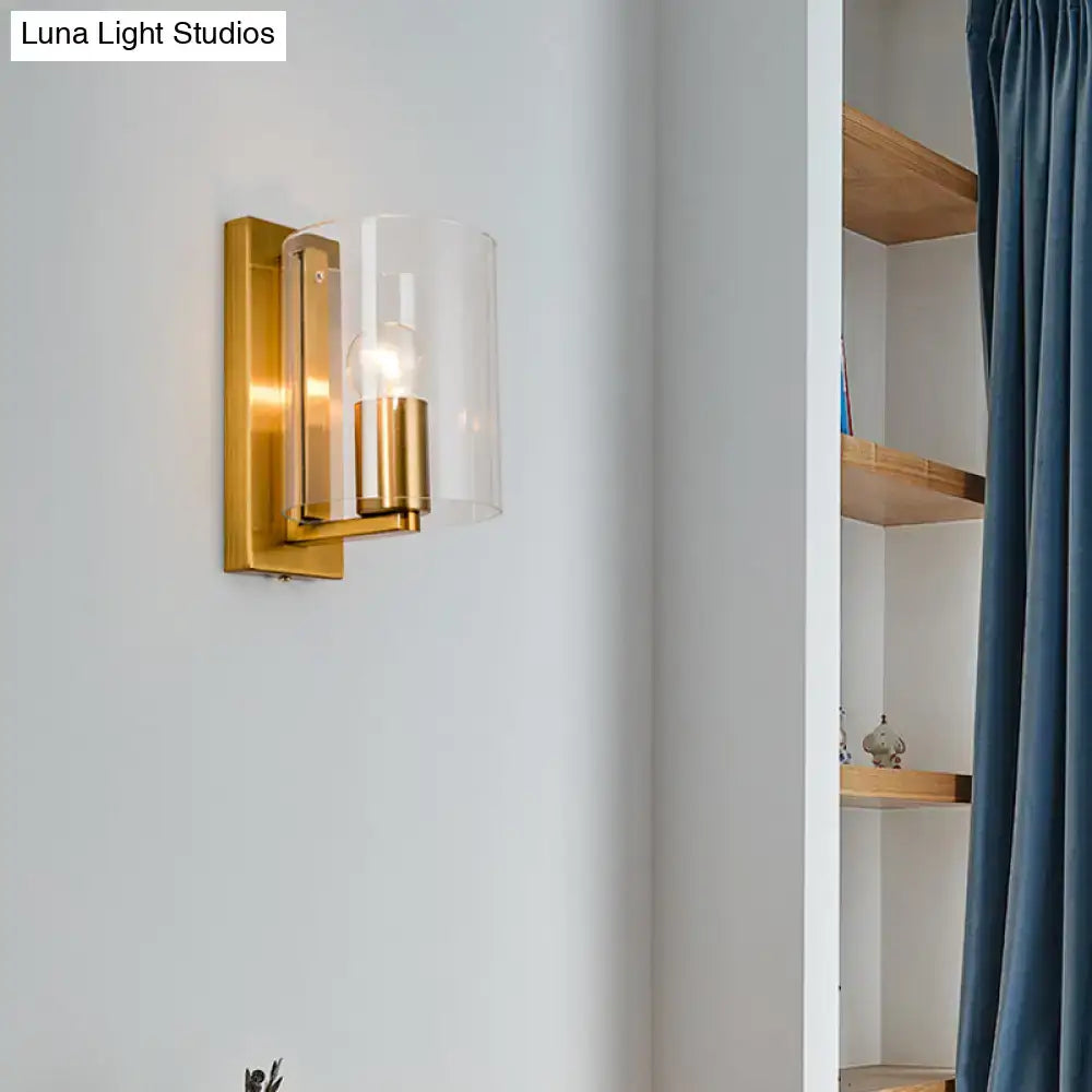 Post modern brass wall sconce with clear textured white glass shade and gold-toned cylindrical brass accents for bedroom use