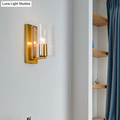 Post modern brass wall sconce with clear textured white glass shade and gold-toned cylindrical brass accents for bedroom use