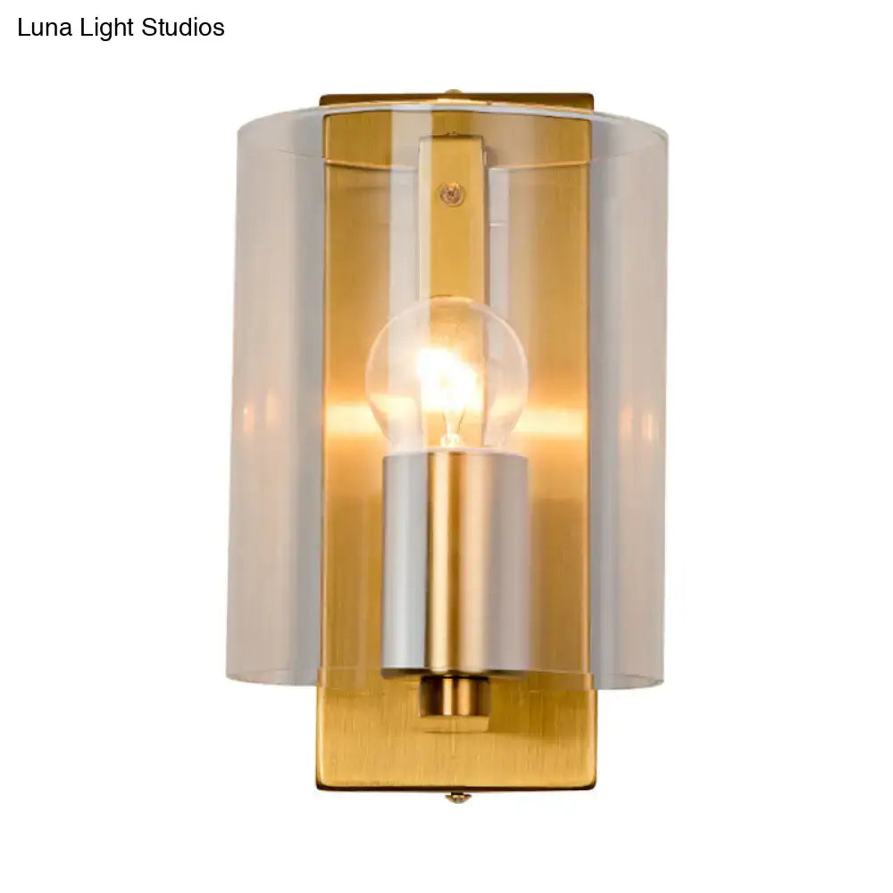 Post modern brass wall sconce with gold-toned finish frosted glass cylinder and clear textured white light for bedrooms