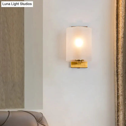 Post modern brass wall sconce with gold finish and clear textured white frosted glass cylinder shade for bedroom lighting