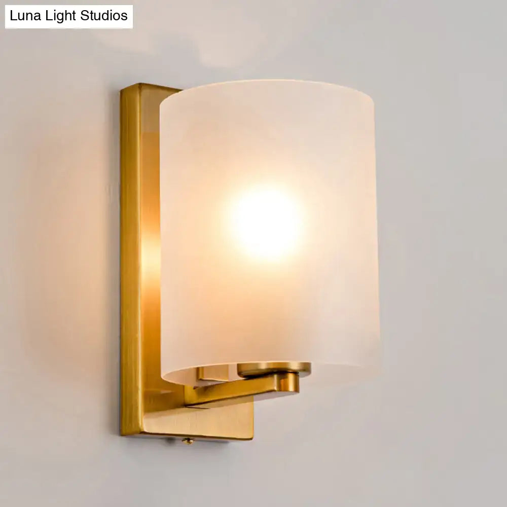 Post modern brass wall sconce with a warm-toned brass finish and clear textured white cylindrical frosted glass shade
