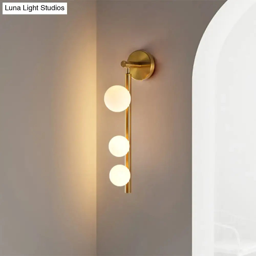 Post modern gold finish wall lamp with three frosted glass globe bulbs arranged vertically on a slender rod