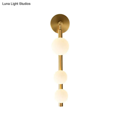 Post modern wall lamp with gold finish featuring three frosted glass spheres on a slender metallic stem