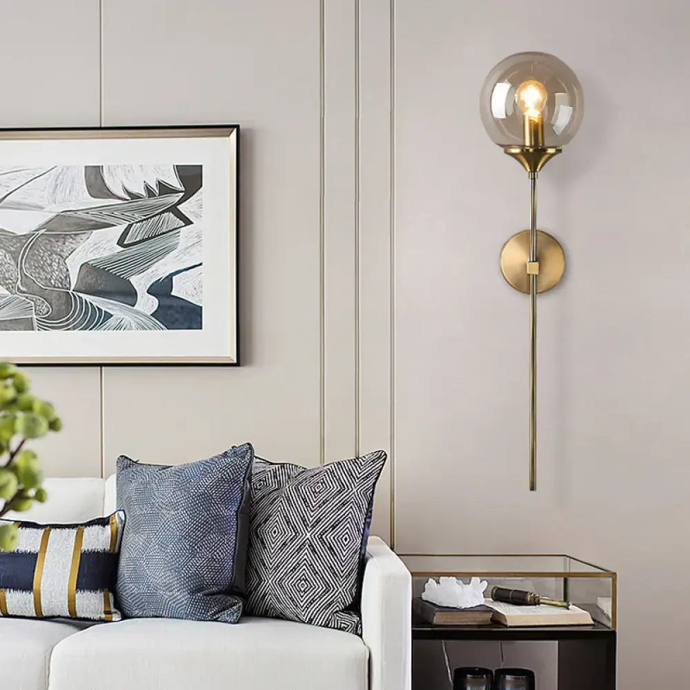A modern wall sconce with smoke grey spherical glass shade and brass base designed for e26 e27 bulb use