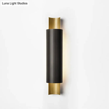 Modern pipe shaped led wall mount with a sleek black cylindrical body and gold-toned accents emitting warm light