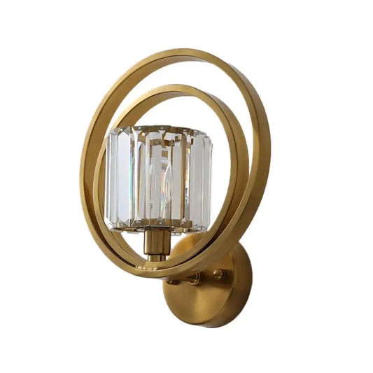 Postmodern brass and crystal drum wall mount light with gold-toned sconce and faceted crystal cylinder encased in rings