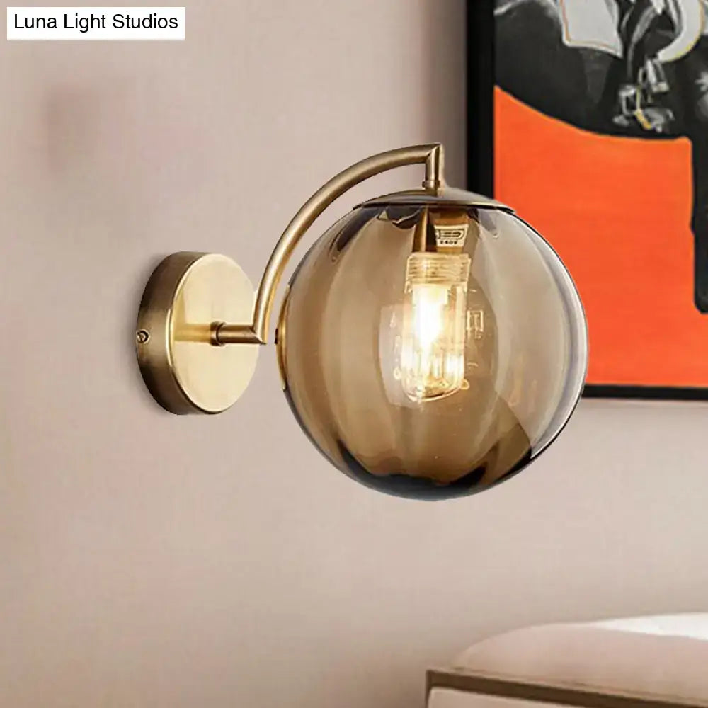 A sleek brass armed ball sconce with a smoked amber glass globe and exposed filament bulb for bedroom lighting