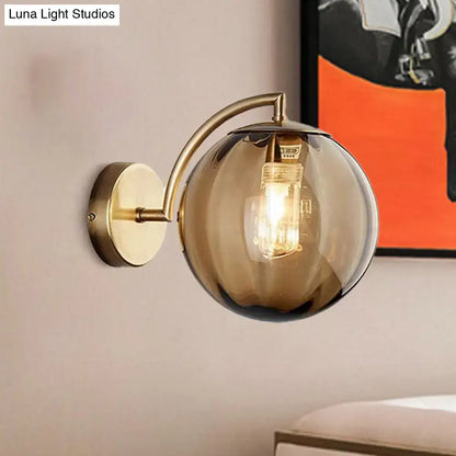 A sleek brass armed ball sconce with a smoked amber glass globe and exposed filament bulb for bedroom lighting