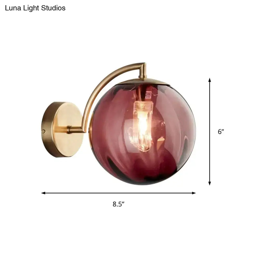 A postmodern brass armed ball sconce with a deep burgundy glass globe for bedroom wall lighting