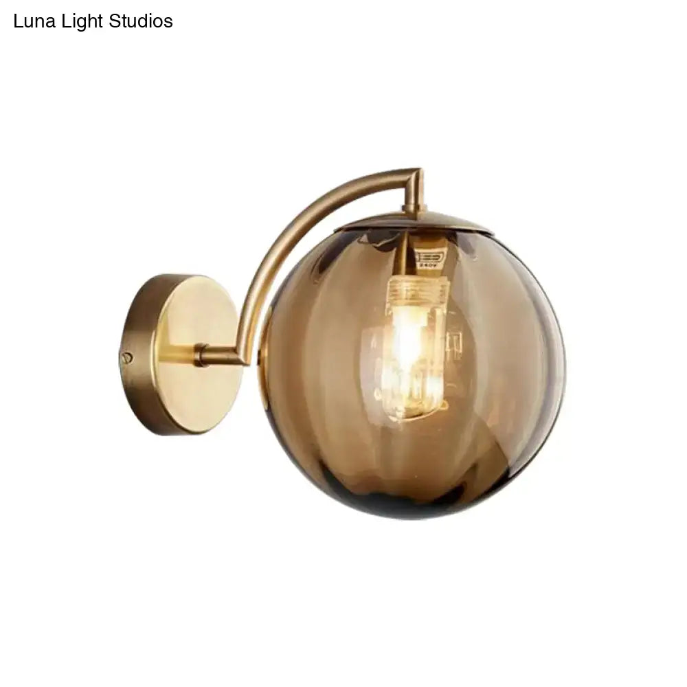 Postmodern brass armed ball sconce with rounded amber glass globe and exposed filament bulb for bedroom lighting