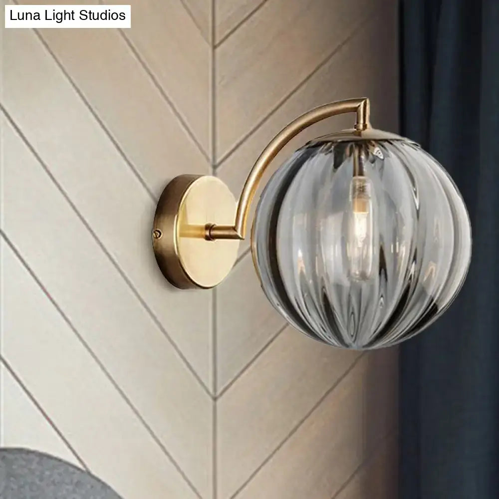 Postmodern brass armed ball sconce with amber glass globe featuring vertical ridges for bedroom wall lighting