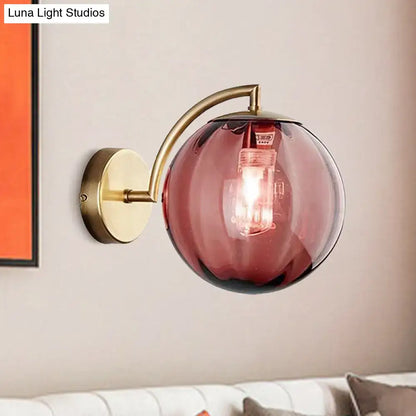Postmodern brass armed ball sconce with a curved arm and amber glass globe for bedroom wall lighting
