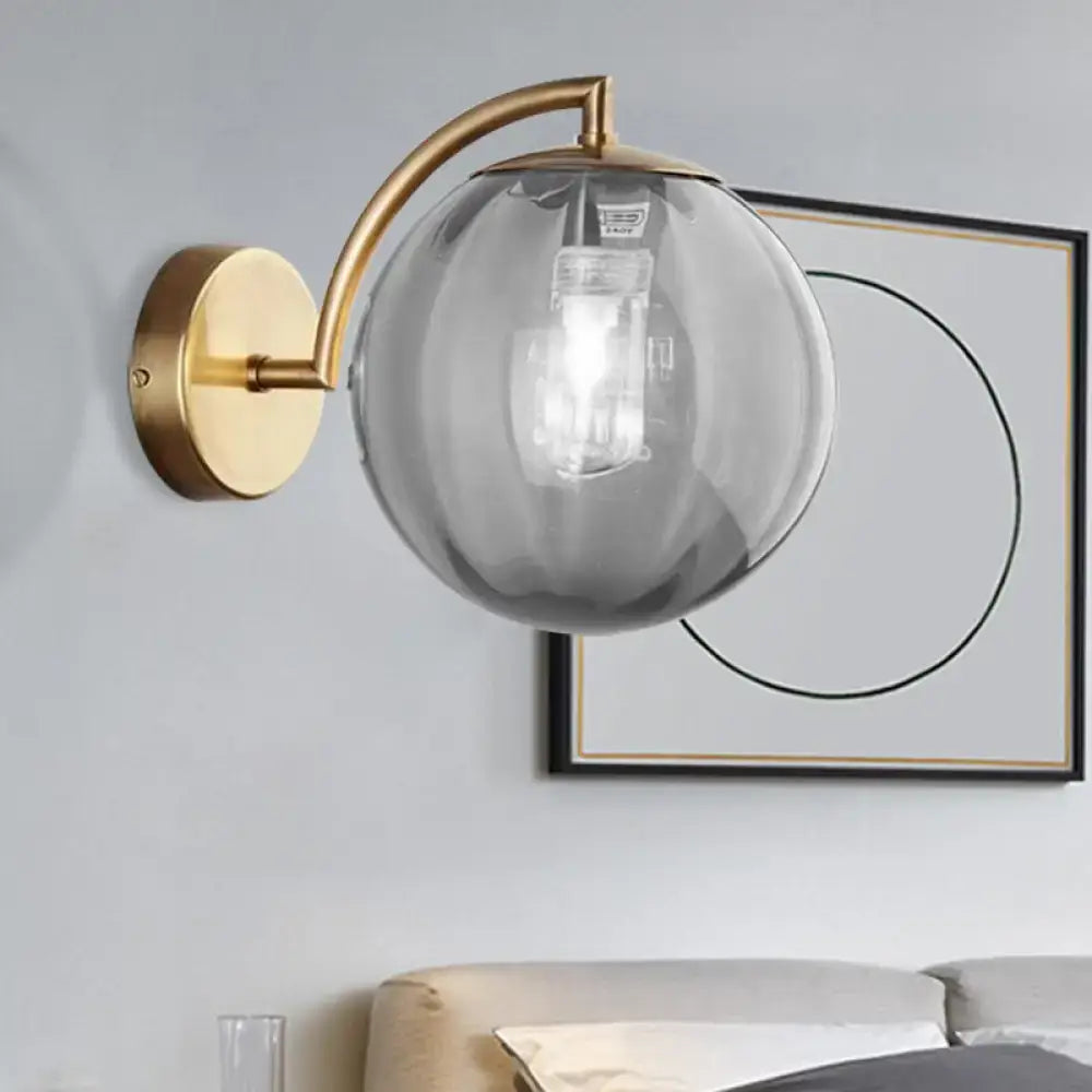 A modern brass armed ball sconce with a brushed finish and amber smoked glass globe for bedroom wall lighting