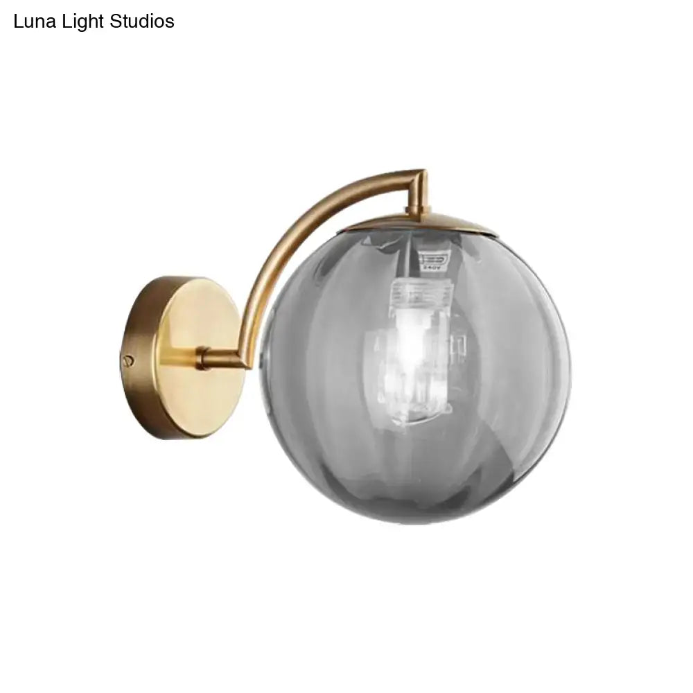 Postmodern brass armed ball sconce with brushed brass mount and amber smoked glass globe for bedroom wall lighting