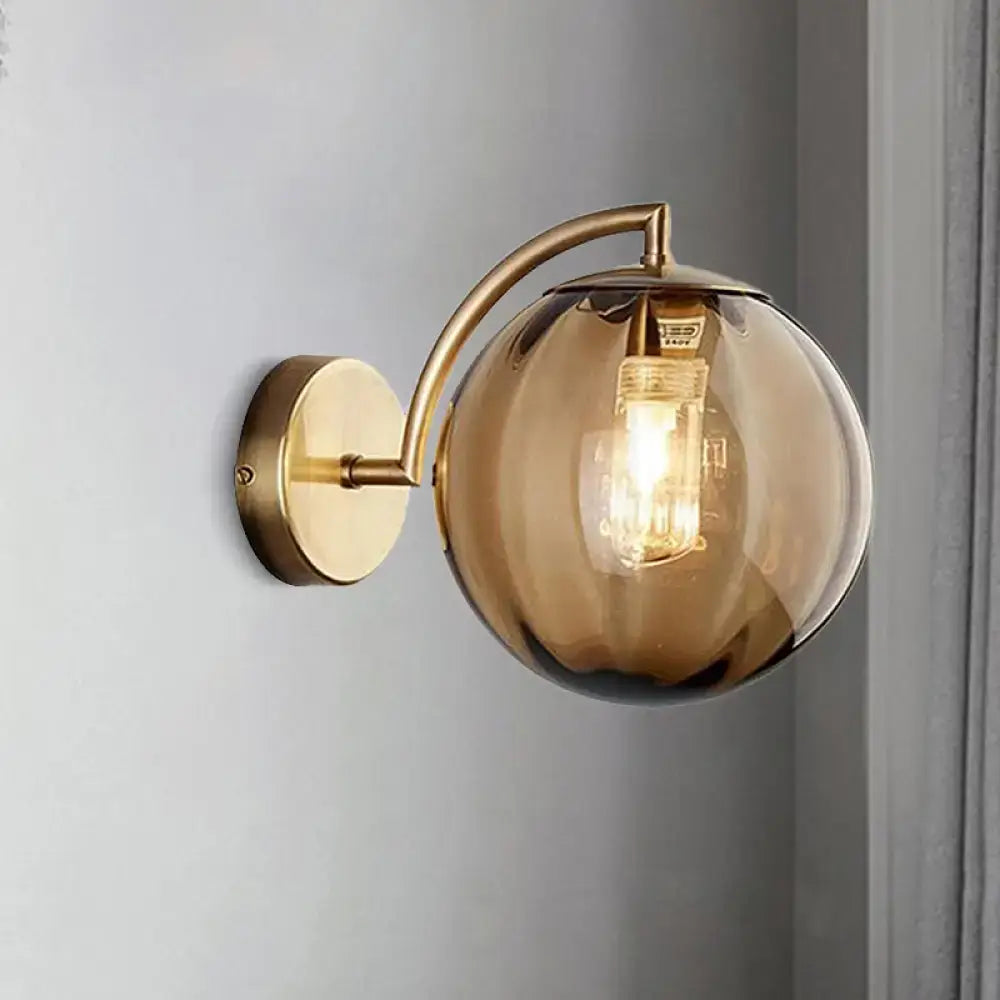 A postmodern brass armed ball sconce with a smoked amber glass globe and exposed filament bulb for bedroom use