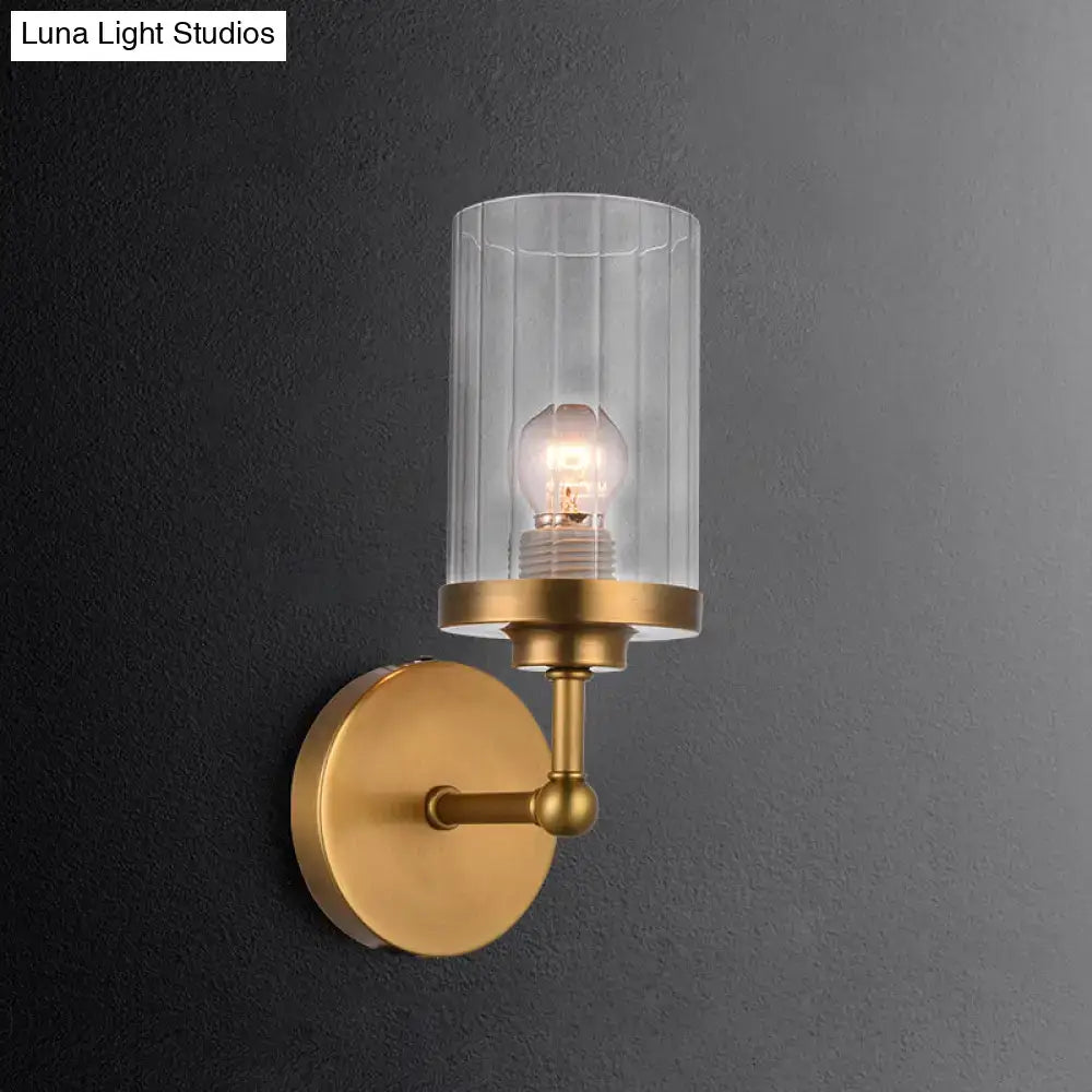 Postmodern brass cylinder wall light with clear vertically ribbed glass and exposed bulb for bedroom use