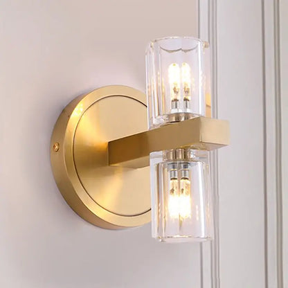 Gold-toned postmodern wall light with brass finish, two clear glass cylinders, and exposed filament bulbs fixture height for bedroom