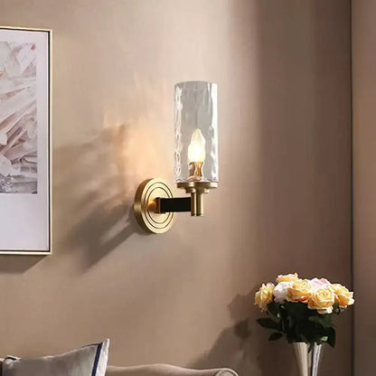 Brass-finished wall mounted light with textured glass cylinder and black accent bar for postmodern living room decor