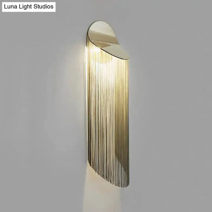 Postmodern gold-toned wall light fixture with sleek curved top and cascading vertical metal strands for bedroom sconce