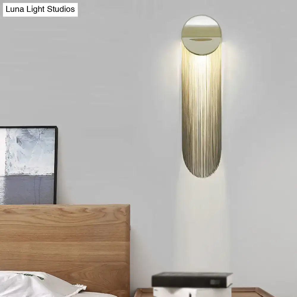 Postmodern gold-toned wall light fixture with elongated oval design and cascading vertical metal strands for bedroom use
