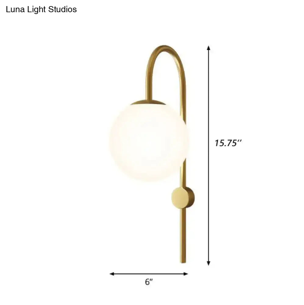 A sleek brass-finished wall lamp with a curved gooseneck arm and cream glass globe for bedroom use
