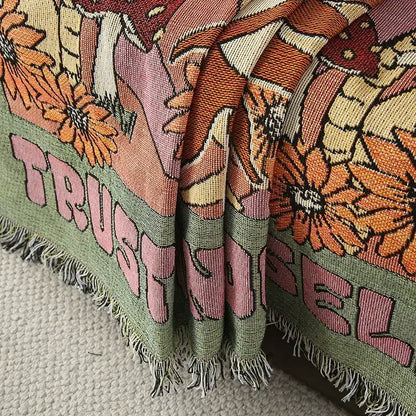 A vibrant ethnic tapestry sofa blanket in olive pink with floral patterns and trust lettering on woven fabric