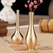 Golden brass mini vintage vases with slender necks and rounded bases one holding dried pink flowers for home decor
