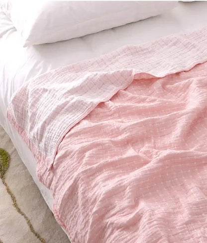 A soft pink quilted grid cotton gauze sofa cover draped over a bed for versatile living room decorbites cotton gauze use